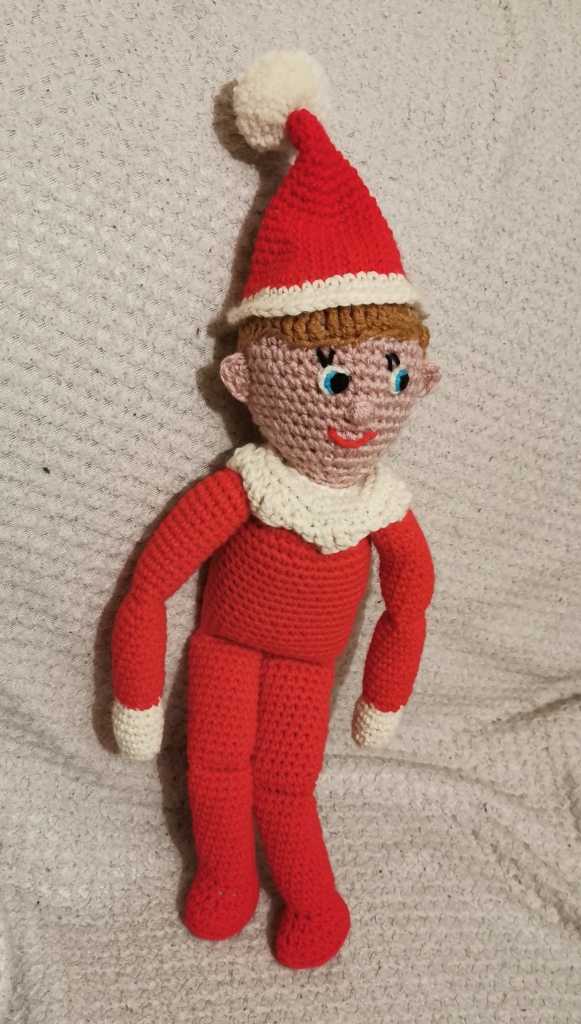 Crochet elf in the shelf. Red body, arms and legs wearing a red hat with a white pompom